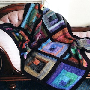 Könnte beinhalten: Eine bunte gestrickte Wolldecke mit einem geometrischen Muster aus Quadraten in Blautönen, Grün, Rot und Braun. Die Decke liegt über einer Chaiselongue.