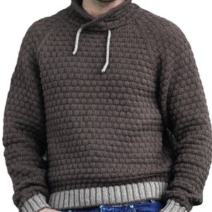 Puede incluir: Un suéter de punto marrón con cuello alto y un patrón texturizado. El suéter tiene un ribete beige alrededor del cuello y los puños.