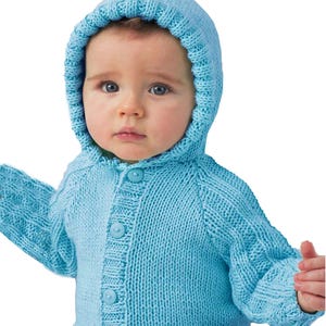May include: A light blue knitted baby hooded cardigan with a button-up front. The sweater has long sleeves and a hood. The baby is wearing white pants. The cardigan is made of a soft, textured yarn.