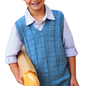 Puede incluir: Un niño pequeño con un chaleco de punto azul sobre una camisa blanca abotonada. Está sosteniendo una barra de pan en una bolsa de papel marrón.