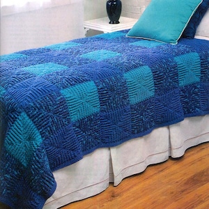 Puede incluir: Una colcha acolchada azul y turquesa con una falda de cama blanca. La colcha tiene un patrón cuadrado con un diseño de remolino.