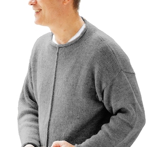 Puede incluir: Un suéter de punto gris de manga larga con cuello redondo, una costura vertical en el centro de la parte delantera y un acabado de dobladillo enrollado en los puños y el borde inferior. El suéter se lleva sobre una camisa blanca y vaqueros azules.
