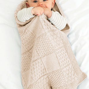 May include: A baby wrapped in a beige knitted blanket with a textured pattern. The blanket has a hood and covers the baby's body, with the baby's face and feet visible. The baby is wearing a striped shirt.