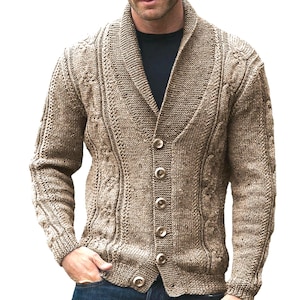 May include: A tan cable-knit cardigan with a shawl collar and button-up closure. The sweater features a textured design and long sleeves. The model is wearing blue jeans and a black shirt underneath the cardigan.