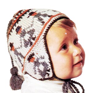 Puede incluir: Un bebé con un gorro de punto blanco, gris y naranja con orejeras y un pompón. El gorro tiene un patrón geométrico.