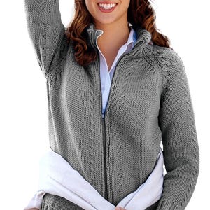 Könnte beinhalten: Graue Strickjacke mit Reißverschluss und hohem Kragen. Die Strickjacke hat einen gerippten Saum und Bündchen, und ein weißes Hemd ist darunter sichtbar. Ein weißer Schal ist um die Taille drapiert.
