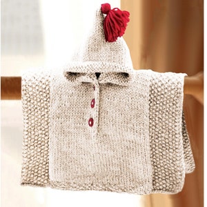 May include: A cream-colored knitted hooded poncho with a red pom-pom on the top of the hood. The poncho has a button closure and is made with a textured stitch.