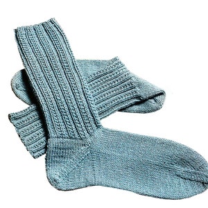 Könnte beinhalten: Ein Paar blaue, gestrickte Socken mit Rippenmuster. Die Socken sind gefaltet und auf einem weißen Hintergrund ausgelegt.