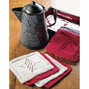May include: Four knitted dishcloths, two white and two red, with a star-shaped design. The dishcloths are stacked on a wooden surface next to a vintage enamel teapot.