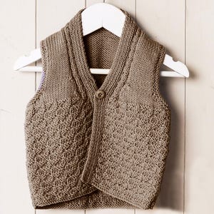 May include: A brown knitted vest with a textured pattern on the front, button closure, and a shawl collar. The vest is hanging on a white hanger against a white wooden background.
