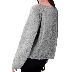May include: A light gray sweater with a textured knit design. The sweater has long sleeves and a scoop neckline. The back of the sweater is visible, showing the knit pattern and the overall shape. The sweater is made of a soft, comfortable material.