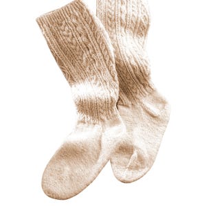 Puede incluir: Un par de calcetines de punto beige con un patrón de trenza. Los calcetines están doblados en la parte superior y están hechos de un material suave y cálido.