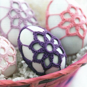 May include: A basket filled with white eggs decorated with crocheted lace. The eggs are decorated with pink, purple, and white lace.