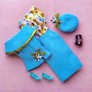 May include: A blue and green doll outfit with a skirt, jacket, hat, and shoes. The jacket has a green trim and a floral brooch. The skirt is a solid blue. The hat is a round blue hat with a green bow. The shoes are blue with a green trim.