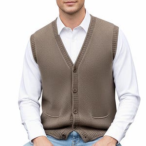 Puede incluir: Un chaleco de punto marrón con cuello en V, cierre de botones y dos bolsillos delanteros. El chaleco se lleva sobre una camisa blanca con cuello y combinado con vaqueros azules. El modelo está sentado en un taburete de madera.