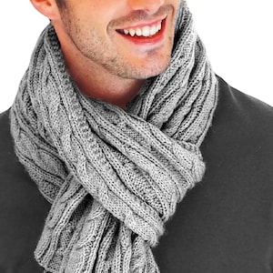 May include: A gray cable knit scarf with a textured pattern. The scarf is folded and worn around the neck.