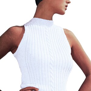 May include: A white, sleeveless ribbed knit top with a high neckline. The top has a central cable knit design and a fitted shape. The model is wearing a black swim cap.