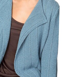 May include: A light blue knitted cardigan with a shawl collar. The cardigan is made of a soft, textured fabric.