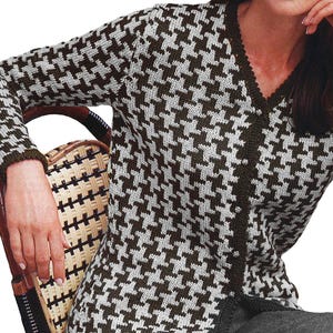 Può includere: Un cardigan a fantasia pied-de-poule marrone e bianco. Il maglione con scollo a V ha maniche lunghe e un'abbottonatura frontale. Il design a maglia presenta un motivo ripetuto di forme marroni e bianche. Il cardigan è indossato sopra un capo scuro.