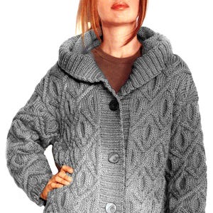 Peut inclure: Un cardigan gris à capuche en tricot torsadé, orné de trois gros boutons. Le pull présente un motif en losanges texturés et un large col. Les manches sont longues, pour un style classique et chaleureux.