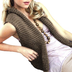 May include: A brown knitted sleeveless vest with a draped neckline. The vest is worn over a light pink top and brown trousers.