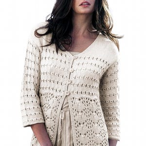 Könnte beinhalten: Cremefarbene Strickjacke mit offenem Vorderteil, V-Ausschnitt und Dreiviertelärmeln. Das Strickwerk hat ein zartes Lochmuster an der unteren Hälfte und den Ärmeln, mit Knopfverschluss. Die Strickjacke hat eine helle, neutrale Farbe.