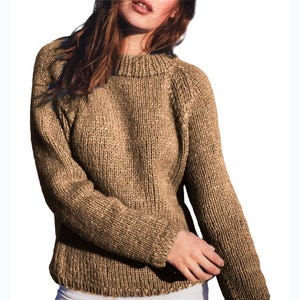 Puede incluir: Un suéter tejido de color marrón claro con cuello alto y mangas largas. El suéter tiene una textura acanalada y un diseño clásico. La prenda está hecha de un material grueso y cálido, ideal para climas más fríos.