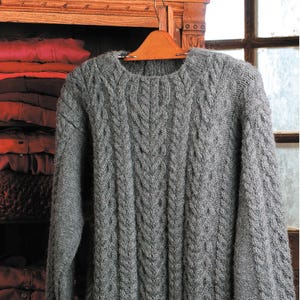 May include: A gray cable knit sweater hanging on a wooden hanger. The sweater has a classic crew neck and is made of a soft, cozy material.