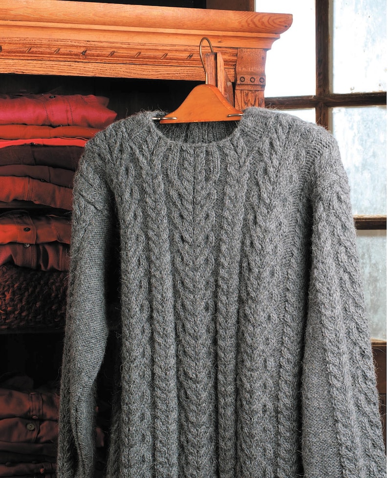 May include: A gray cable knit sweater hanging on a wooden hanger. The sweater has a classic crew neck and is made of a soft, cozy material.