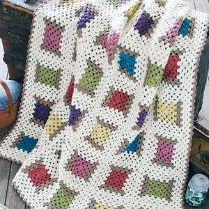 May include: A crocheted blanket with a white background and colorful granny squares. The squares are in shades of pink, red, purple, blue, green, and yellow.