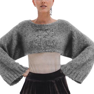 May include: A gray cropped sweater with long sleeves. The sweater is made of a soft, fuzzy material.