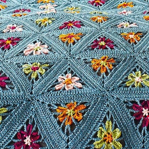 Könnte beinhalten: Nahaufnahme einer gehäkelten Decke mit einem sich wiederholenden Blumenmuster. Die Blumen sind in Rosa-, Orange-, Gelb- und Weißtönen gehalten und vor einem türkisblauen Hintergrund platziert. Die Decke ist aus Garn.