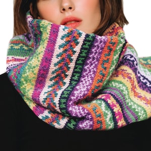 May include: A multi-coloured knitted cowl scarf with a striking pattern. The scarf displays stripes of green, purple, pink, orange, and yellow. The cowl is wrapped around the neck, highlighting the detailed design and texture of the knit.