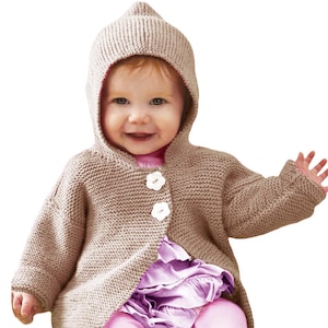 Pode incluir: Um cardigan com capuz de malha bege para bebé, com capuz pontudo e dois botões brancos em forma de flor. O bebé usa um top rosa e uma saia roxa.