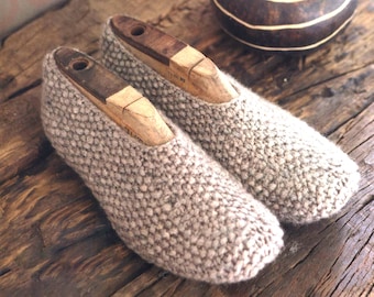 Puede incluir: Un par de zapatillas de punto beige con hormas de madera en su interior. Las zapatillas están sobre una superficie de madera.