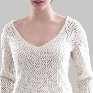 Puede incluir: Suéter de manga larga color crema con cuello en V profundo. El suéter presenta un diseño de crochet con patrón de diamantes. Las mangas son largas y ajustadas, y el escote es amplio. El suéter está hecho de un material suave y texturizado.