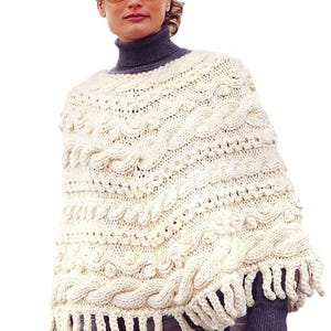 May include: A white knitted poncho with a cable knit pattern and fringe trim.