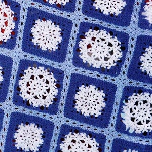 May include: A blue and white crocheted blanket with a snowflake pattern. The blanket is made of squares with a white snowflake in the centre of each square.