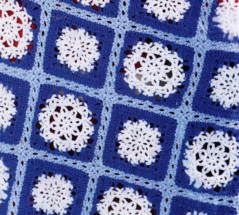 May include: A blue and white crocheted blanket with a snowflake pattern. The blanket is made of squares with a white snowflake in the centre of each square.