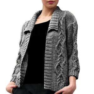 Op de afbeelding: Een grijze kabelgebreide cardigan met een sjaalkraag en driekwart mouwen. De open trui heeft een textuurontwerp en wordt over een zwarte top gedragen. De cardigan is van gemiddeld gewicht en lijkt gemaakt van wol of een wolmix.