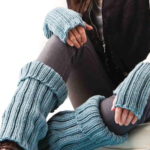 Puede incluir: Un conjunto de calentadores de piernas y guantes sin dedos de punto azul claro. El tejido de punto acanalado es de un color azul suave y apagado. Los calentadores de piernas están doblados en la parte superior. Los guantes tienen un puño acanalado y dedos abiertos.