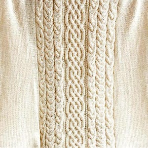Pode incluir: Cobertor de malha creme com um design central de malha de cabo. O cobertor apresenta um padrão texturizado com pontos de cabo verticais e uma borda de malha lisa. O design geral é simétrico e aconchegante, perfeito para decoração de casa.