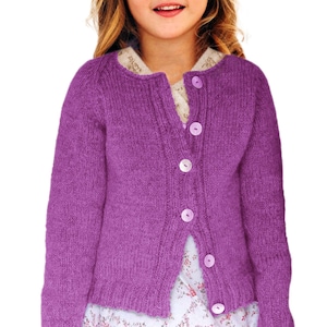 Puede incluir: Un cárdigan de punto morado con cuello redondo y mangas largas. El cárdigan tiene cinco botones blancos en la parte delantera. La prenda está hecha de un hilo suave y texturizado. Es una prenda infantil.