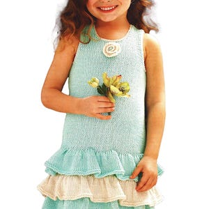 May include: A light blue knitted dress with a tiered ruffle skirt. The dress has a round neckline with a white flower embellishment and is sleeveless. The girl is holding a small bouquet of yellow flowers.