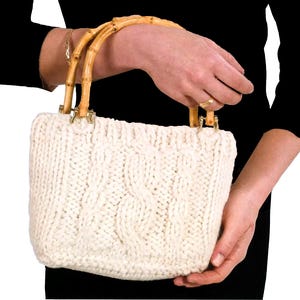 May include: A white knitted handbag with bamboo handles. The bag has a cable knit pattern.