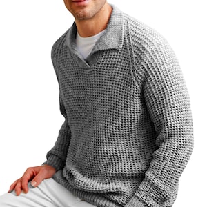 Puede incluir: Un suéter gris de punto de waffle con cuello. El suéter tiene un corte holgado y mangas largas.