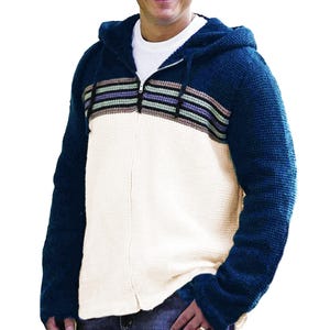 May include: A blue, cream, and striped zip-up hoodie. The hoodie has a navy blue hood and sleeves, a cream-coloured body, and a horizontal stripe design across the chest. The stripes include shades of green, purple, and brown.