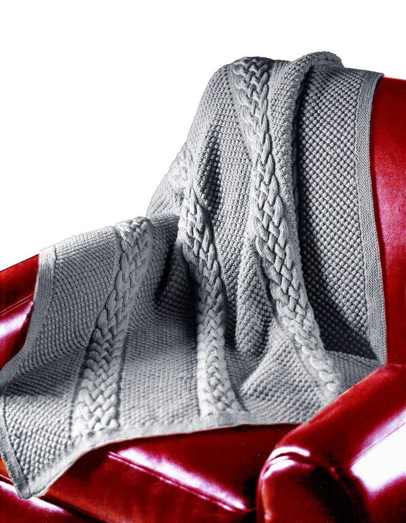 Puede incluir: Una manta de punto de cable gris con un patr&oacute;n texturizado est&aacute; drapeada sobre un sill&oacute;n de cuero rojo.