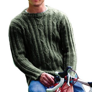 May include: A green knit sweater with a crew neck and cable knit detailing. The sweater has a ribbed texture and long sleeves. The person is wearing blue jeans and holding a bicycle.