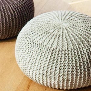 May include: Two knitted poufs, one in a light beige color and the other in a dark brown color. The poufs are round and have a textured surface.